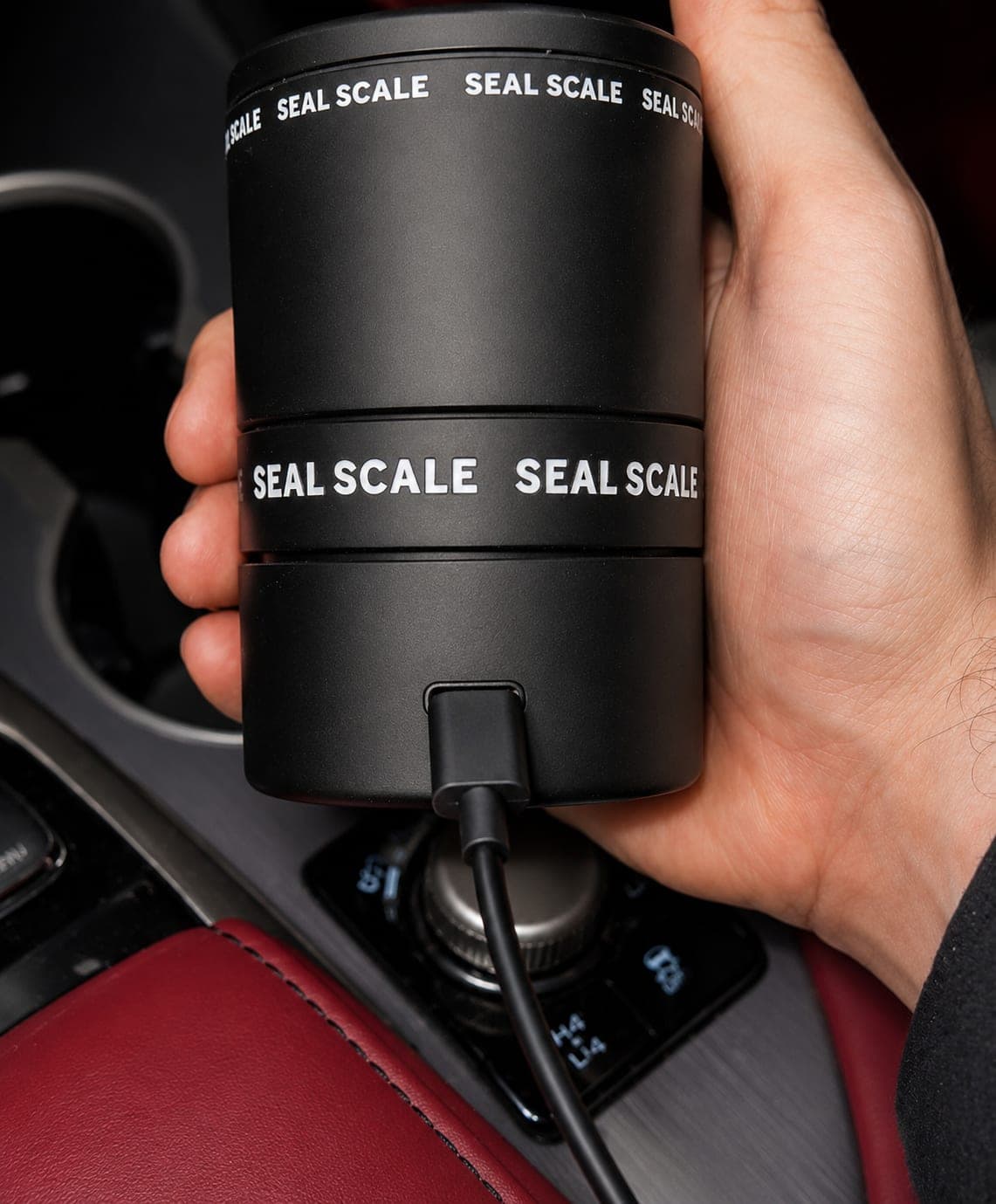 Seal Scale airtight container held in one hand inside a car, recharging through its USB-C port on the back